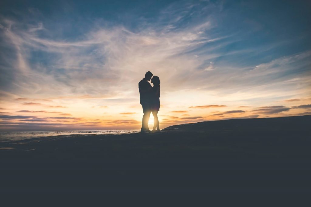 Un couple s'embrasse tendrement alors que le soleil se couche derrière eux, créant une atmosphère chaleureuse et romantique.