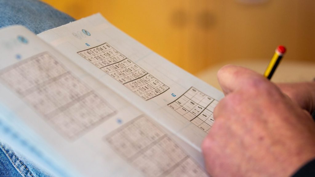 Personne résolvant un puzzle Sudoku sur une table.